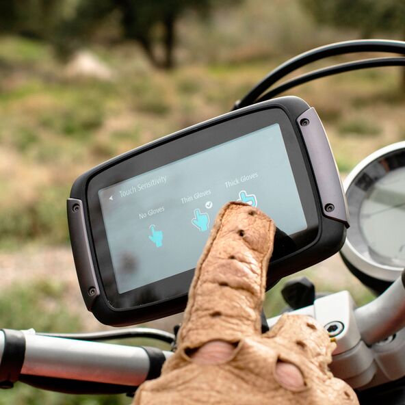 Motorrad-Navi mit Touchscreen im Querformat, montiert an einem Motorradlenker, mit Kartendarstellung auf dem Display. Der Hintergrund zeigt eine Landschaft.