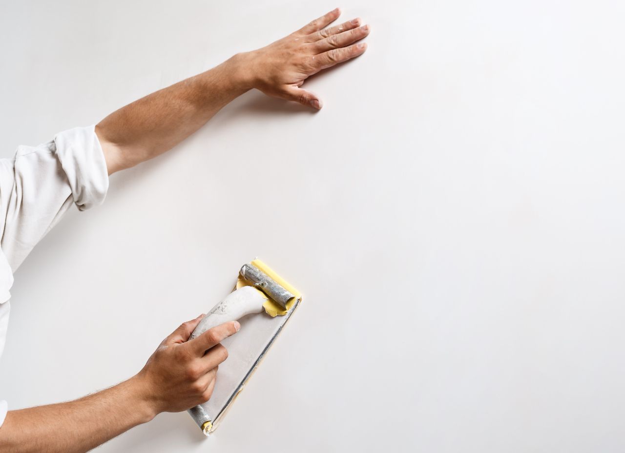 Mann der eine weiße Wand mit Sandpapier schleift