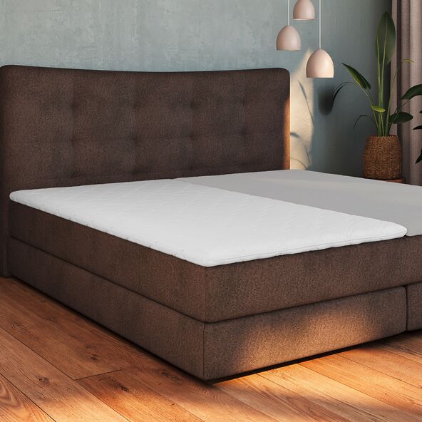 Matratzen Topper Basis, 100 x 200 cm, ausgerollt auf einem Bett liegend. Die weiße, gesteppte Oberfläche ist leicht strukturiert.