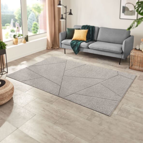Der Teppich mit Hochflor-Muster zeigt ein abstraktes, helles Muster auf beigem Grund. Der Flor wirkt weich und dicht.
