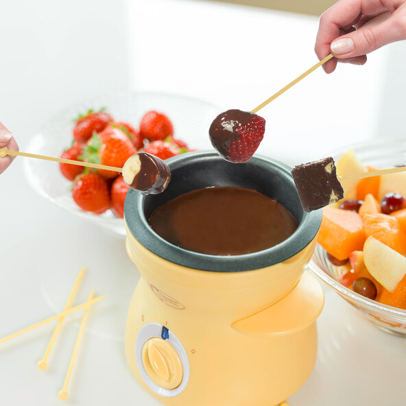 Gelbes Mini Schoko-Fondue Set mit Keramikschälchen, Teelicht und zwei Gabeln, vor weißem Hintergrund präsentiert.