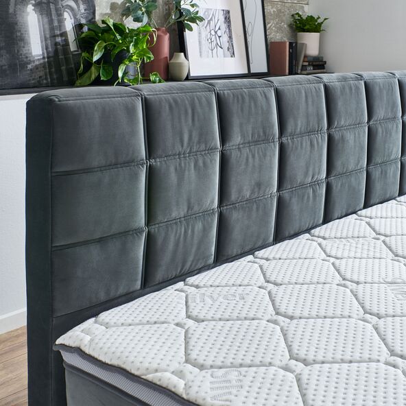 Anthrazitfarbenes Boxspringbett Premium, bestehend aus Matratze, Topper und Unterbau. Das Bett steht auf dunklen Füßen und hat ein gepolstertes Kopfteil.