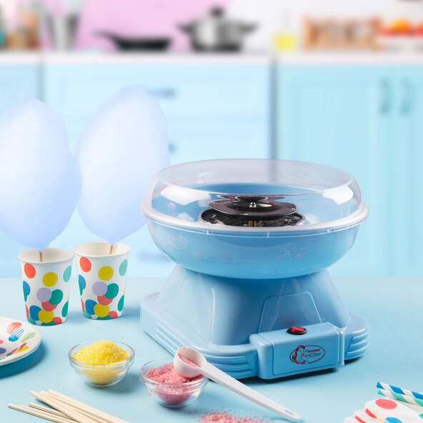 Blaue Zuckerwattemaschine mit transparentem Spritzschutz. Der Behälter ist weiß und enthält rosa Zuckerwatte. Ein Messlöffel liegt daneben.
