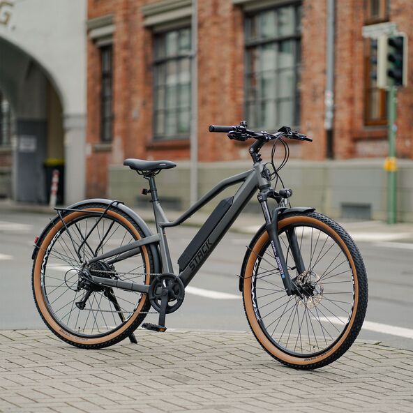 Schwarzes Stack Sport E-SUV Bike 29" mit orangefarbenen Akzenten, Seitenansicht, im Freien vor verschwommenem Hintergrund.
