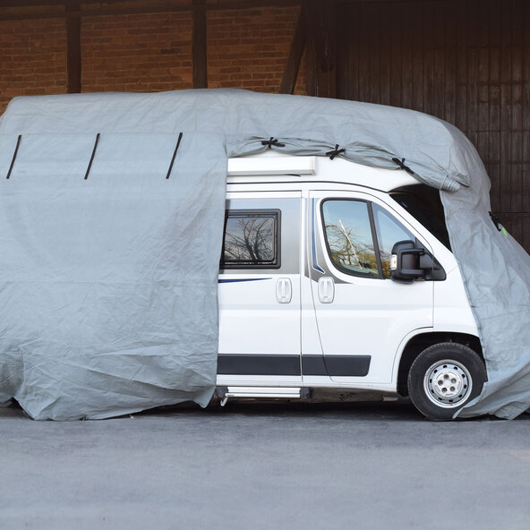 Wohnmobil Schutzhülle in hellem Grau, über ein weißes Wohnmobil gezogen. Die Hülle ist passgenau und schützt das Fahrzeug vor Witterungseinflüssen.
