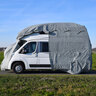 Wohnmobil Schutzhülle in Grau. Das Wohnmobil ist vollständig bedeckt und steht im Freien vor Bäumen und Büschen.