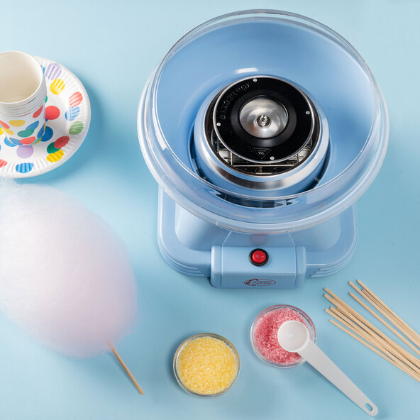 Blaue Zuckerwattemaschine mit transparentem Spritzschutz und Auffangschale, stehend auf einem Tisch, zur Herstellung von Zuckerwatte.