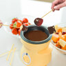 Gelbes Mini Schoko-Fondue Set mit Keramikschälchen, Teelicht und zwei Gabeln, vor weißem Hintergrund präsentiert.