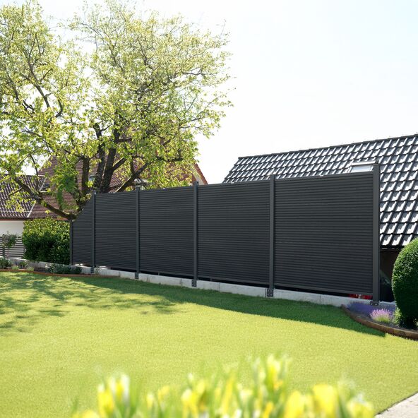 Ein CALLADO Premium Zaunpfosten, der robust im Boden verankert ist, mit einem dichten, grünen Garten im Hintergrund.