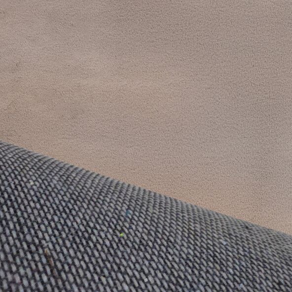 Sandfarbener, rechteckiger Teppich mit dichter, weicher Oberfläche. Der Teppich liegt flach auf einem hellen Untergrund und füllt fast das gesamte Bild aus.
