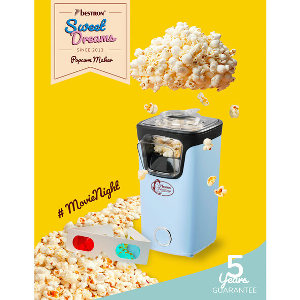 Blaue Popcornmaschine mit transparentem Behälter und rotem Messlöffel, steht auf einer weißen Oberfläche. Das Produkt wirkt neu und unbenutzt.