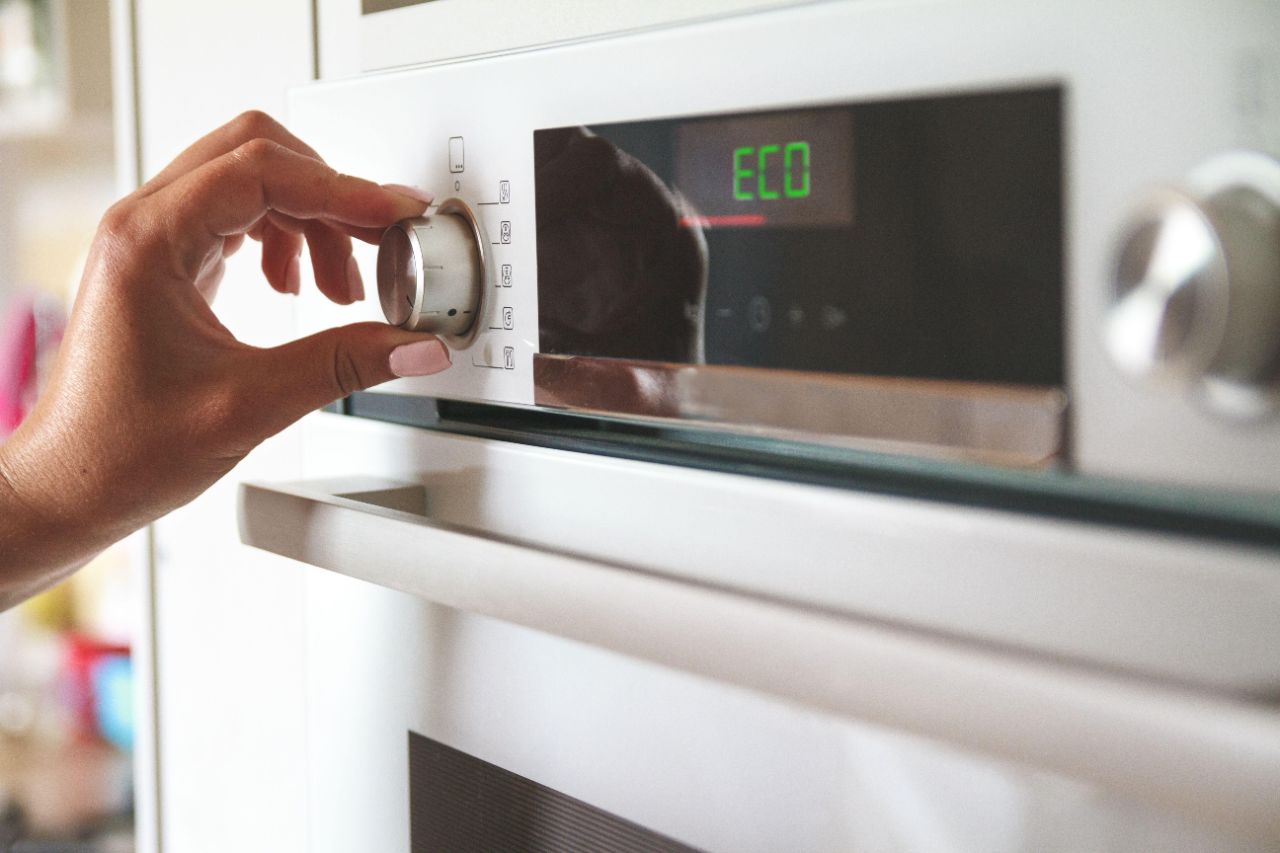 Eine Frau mit rosa Fingernägeln wählt den Eco-Modus an einem weißen Backofen über einen Drehregler aus