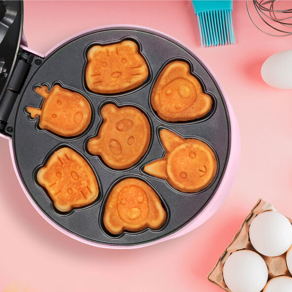 Ein pinkfarbener Mini Cookie Maker mit Herzform-Aussparungen auf einer weißen Oberfläche, frontal fotografiert. Mehrere fertig gebackene Kekse liegen daneben.