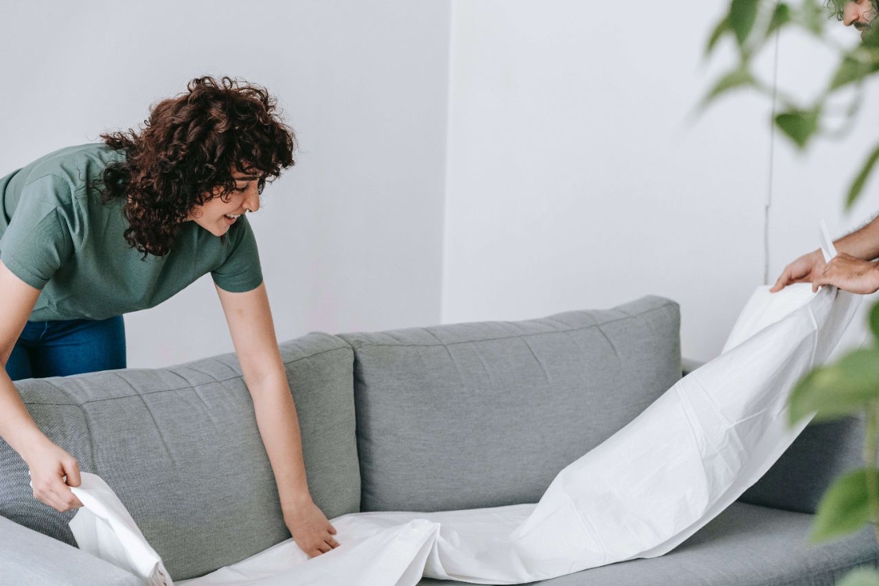Eine Frau und ein Mann bedecken gemeinsam eine graue Couch mit einem weißen Tuch