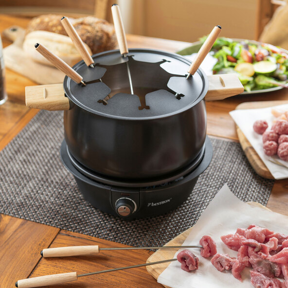 Fondue Set bestehend aus Topf, Rechaud, acht Gabeln mit farbigen Griffen und Spritzschutz, aufgebaut auf einem Tisch.
