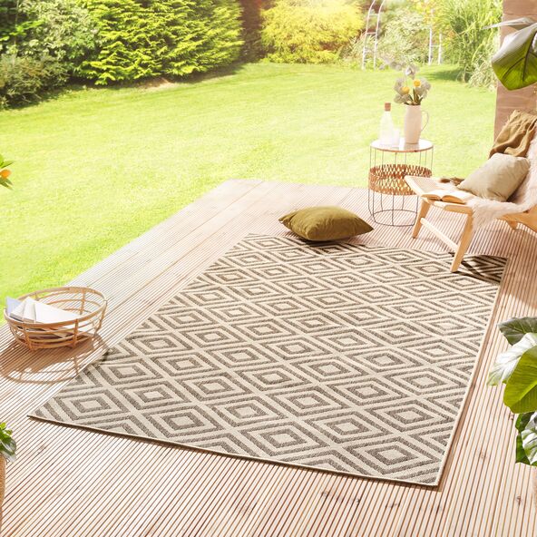 Ein rechteckiger Outdoor-Teppich mit geometrischem Muster in Grau- und Beigetönen liegt auf einer Terrasse oder einem Balkon.
