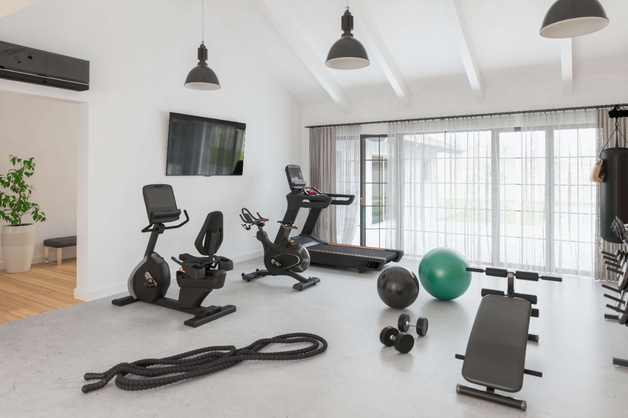 Modern eingerichtetes Home-Gym in Schwarz-Weiß-Grau mit TV, Klima, Laufband, Fahrrad, Hantelbank, Hanteln und Gymnastikbällen