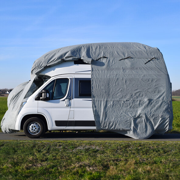 Wohnmobil Schutzhülle in Grau. Das Wohnmobil ist vollständig bedeckt und steht im Freien vor Bäumen und Büschen.