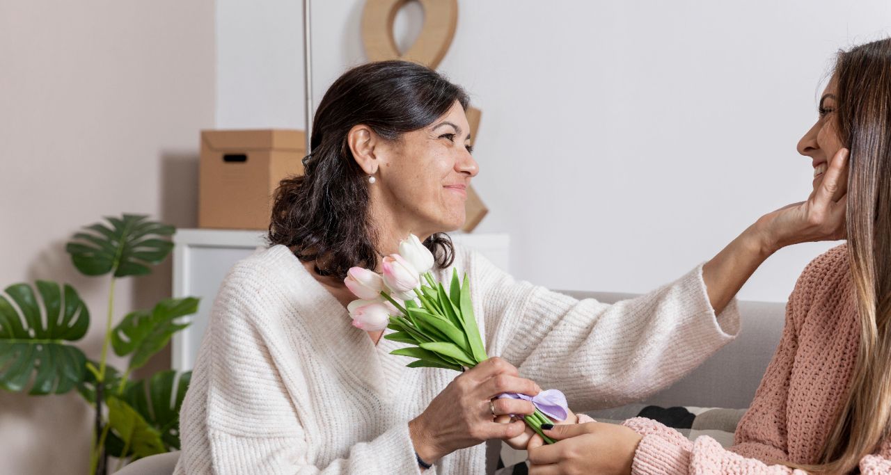 Eine Mutter bekommt von ihrer Tochter weiße Tulpen geschenkt und kneift ihr leicht in die Wangen