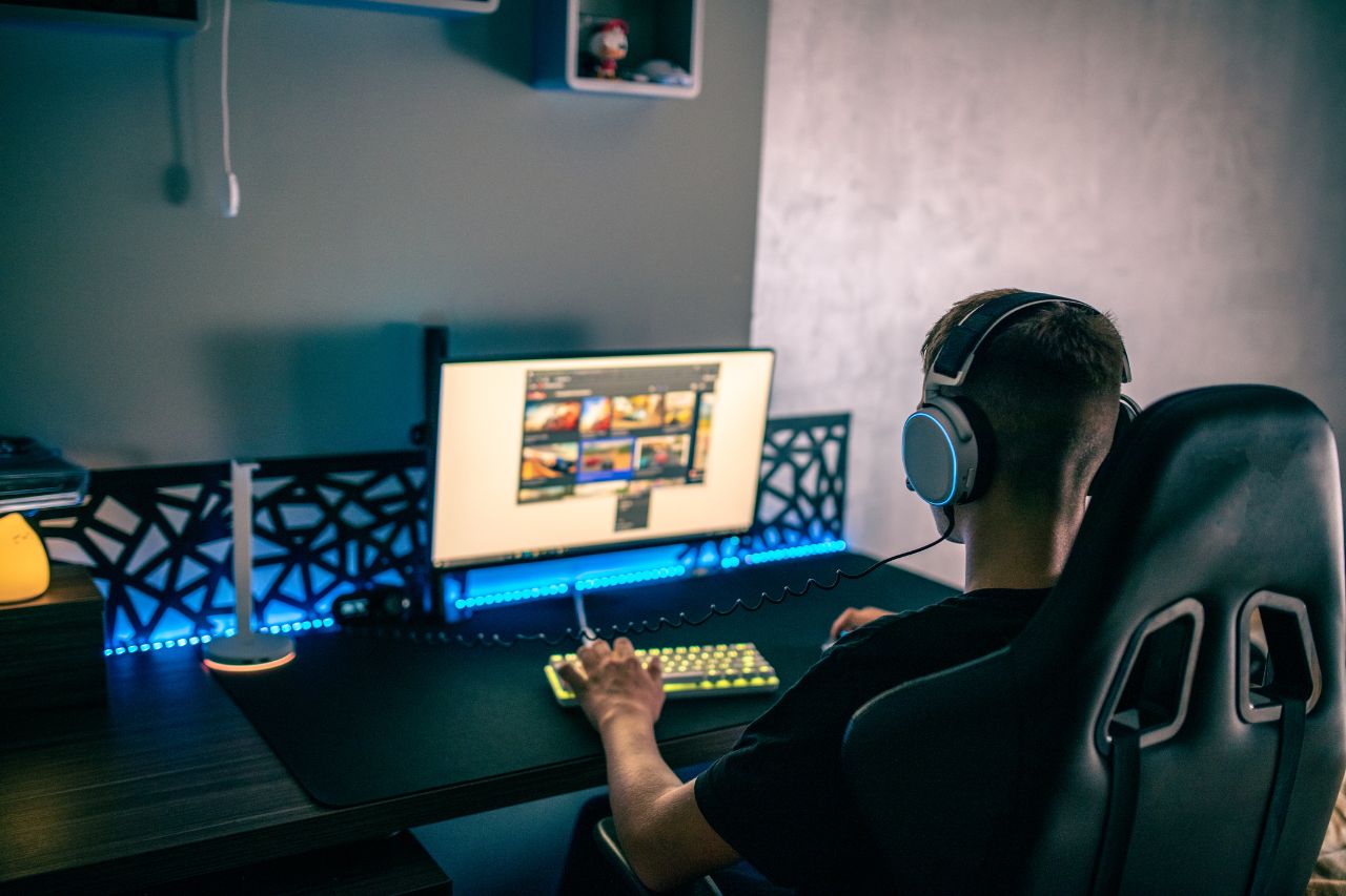 Ein junger Mann mit Headset sitzt an seinem Gamingschreibtisch und spielt ein Computerspiel