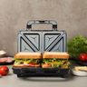 Silberner Sandwichmaker mit geriffelten Heizplatten, geschlossen dargestellt. Zwei Toast-Sandwiches sind leicht erkennbar. Das Gehäuse ist aus Metall.