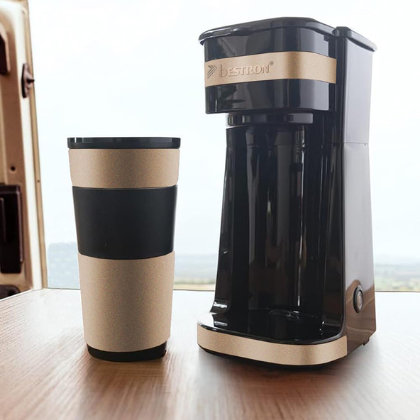 Beige, kompakte Kaffeemaschine mit Thermobecher steht auf einer weißen Oberfläche. Die Kaffeemaschine hat einen schwarzen Deckel und der Becher ist beige.