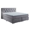 Hellgraues Boxspringbett, bestehend aus Matratze und Topper auf einem gefederten Untergestell. Das Bett ist mit einem hohen, gesteppten Kopfteil ausgestattet und steht auf dunklen Füßen.
