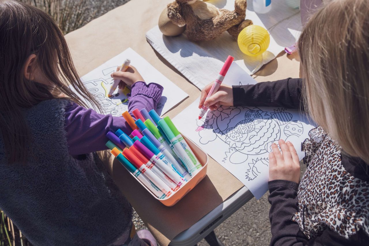 Zwei Kinder sitzen draußen an einem Tisch und malen ein Bild mit bunten Stiften aus