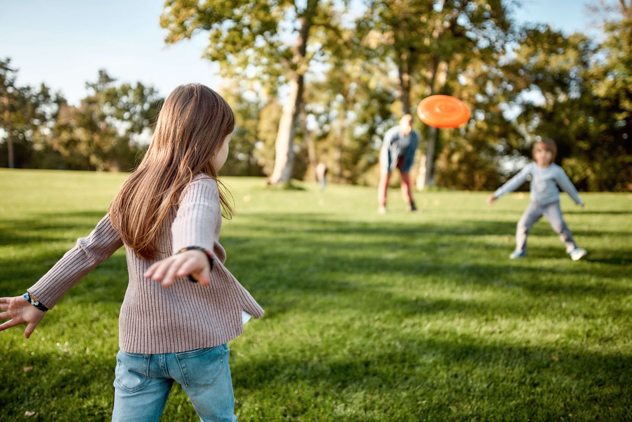 Zwei Kinder spielen bei schönem Wetter auf der grünen Wiese mit einer orangen Frisbee