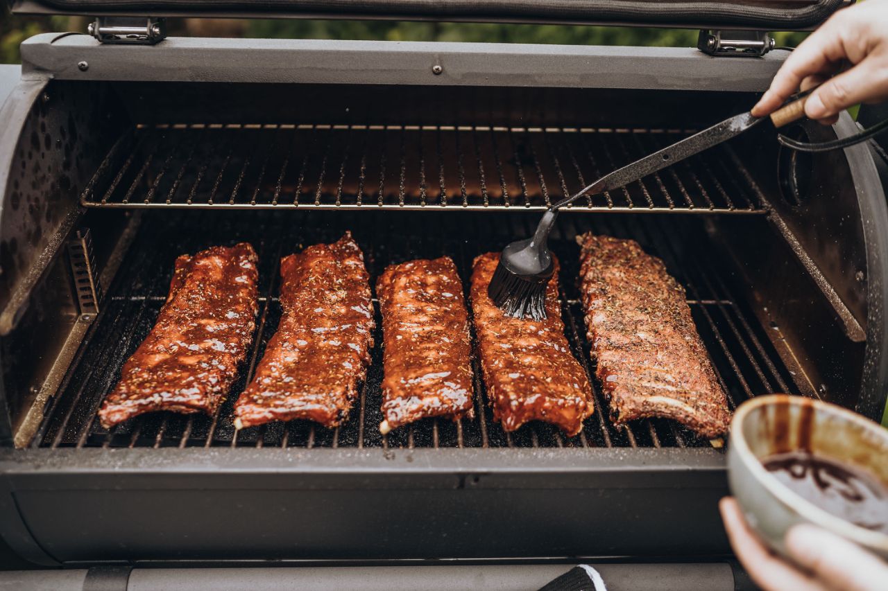 Mehrere Spare Ribs liegen auf dem Grill und werden mit einer flüssigen Marinade bestrichen.