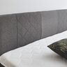 Graues Boxspringbett Basic mit großem Kopfteil, bestehend aus Matratze und Unterbau, im Schlafzimmer vor heller Wand.