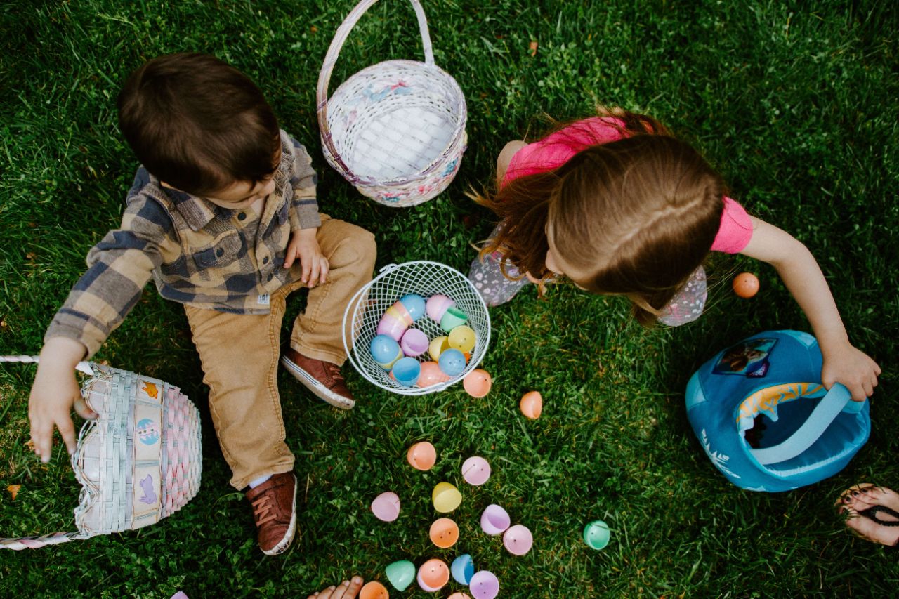 Zwei Kinder sitzen auf der grünen Wiese und spielen mit Osterkörben und bunten Plastik-Eiern
