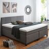 Graues Boxspringbett Basic mit großem, rechteckigem Kopfteil und strukturierter Oberfläche, im Schlafzimmer auf hellem Holzboden stehend.