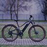 Dunkelblaues E-Mountainbike mit 29-Zoll-Reifen, Federgabel und sportlicher Rahmengeometrie, abgebildet vor hellem Hintergrund.