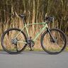 Resedagrünfarbenes Gravel Bike GravelerFit mit schwarzem Sattel und Lenker, stehend auf unbefestigtem Untergrund. Fokus liegt auf dem Fahrradrahmen und den Reifen.
