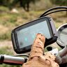 Motorrad-Navi mit Touchscreen im Querformat, montiert an einem Motorradlenker, mit Kartendarstellung auf dem Display. Der Hintergrund zeigt eine Landschaft.